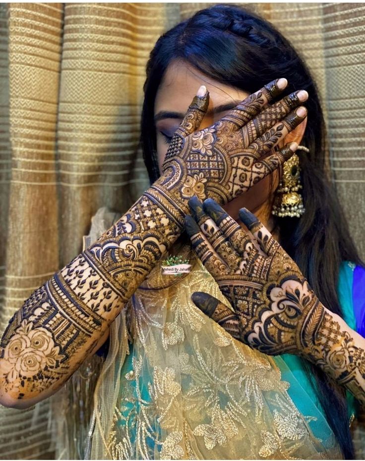 This may contain: a woman holding her hands up to her face with henna tattoos on it's arms