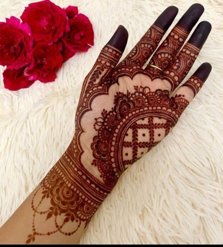 This may contain: a henna on someone's hand next to some red flowers and a rose