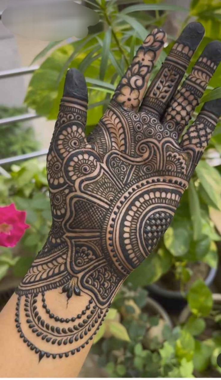 This may contain: a hand with henna on it in front of some plants and flowers at the bottom