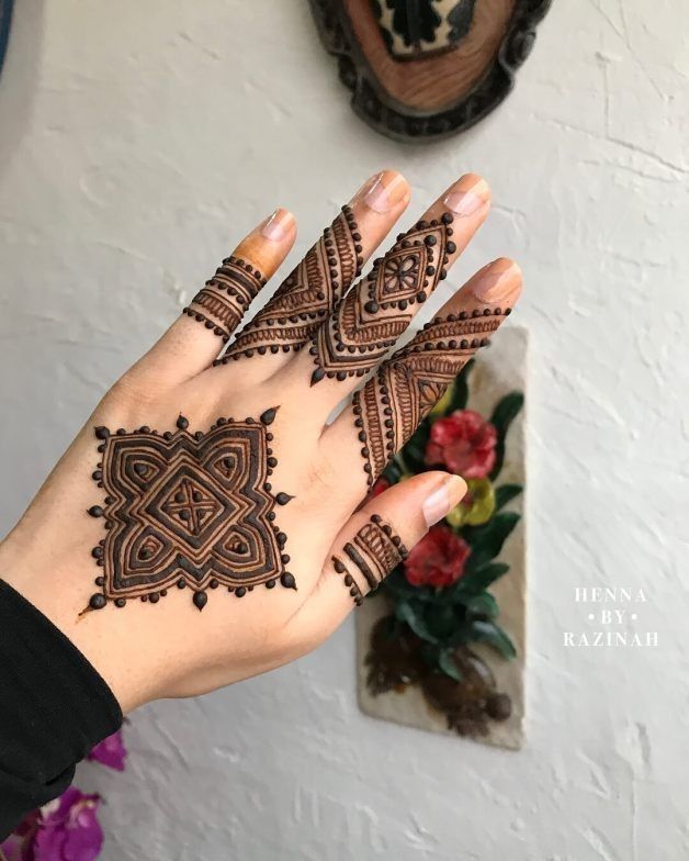 This may contain: a woman's hand with henna tattoos on it and flowers in the background