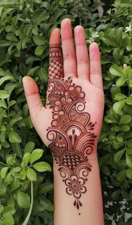 This may contain: someone's hand with henna on it and green plants in the back ground