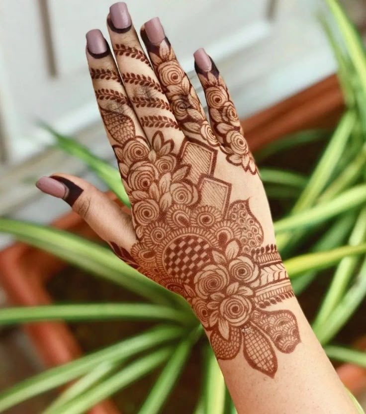 This may contain: a woman's hand with henna on it and some plants in the background